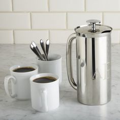 two mugs with spoons are sitting next to each other on a marble counter