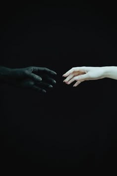 two hands reaching out towards each other on a black background with one hand holding the other's hand