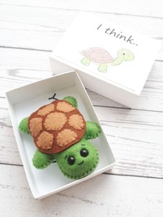 a small green turtle in a white box next to a thank you card and envelope