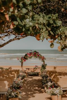 an outdoor ceremony set up on the beach with flowers and greenery in front of it