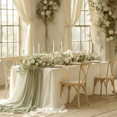 a long table with white flowers and candles on it in front of two large windows