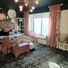 a bedroom decorated in pink and black with an ornate bed, chandelier, window seat, and chair