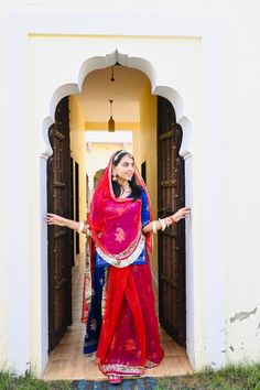 a woman in a red and blue sari is posing for the camera with her arms outstretched