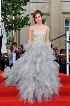 a woman in a gray dress standing on red carpet next to stairs with people taking pictures