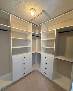 an empty walk in closet with white shelves and drawers