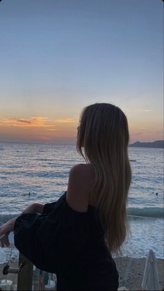 a woman standing on top of a sandy beach next to the ocean at sun set