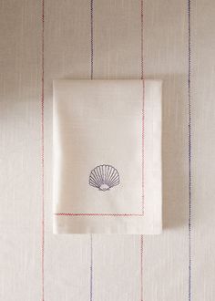 an embroidered napkin with a seashell on it sits next to a striped wallpaper