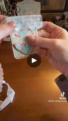 two hands holding up a piece of paper on top of a wooden table with lace