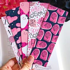 the hand is holding four pink and blue bookmarks