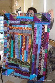 a woman holding up a very large colorful quilt