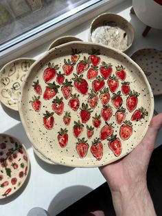 a hand holding a plate with strawberries on it and other plates in the background