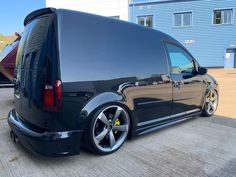 the back end of a black van parked in front of a blue building with windows