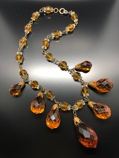 an orange and yellow necklace on a black surface with gold chains, beads and crystal drops