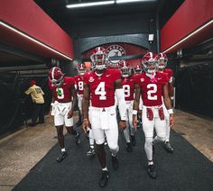 three football players are walking down the tunnel together in uniforms with numbers on their jerseys