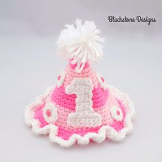 a crocheted pink and white hat with the number 1 on it's side