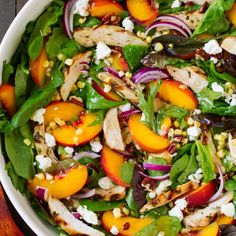 a salad with peaches, spinach and feta cheese in a white bowl