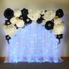 an arrangement of white and black flowers on a sheer curtained backdrop with fairy lights