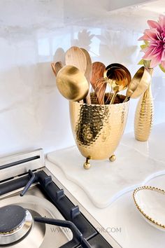 a gold vase with spoons and other kitchen utensils on a stove top