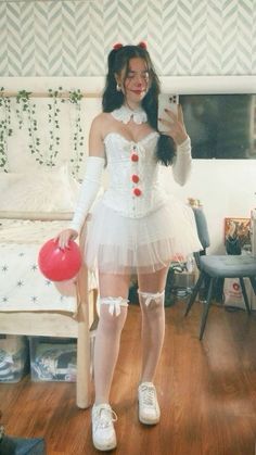 a woman dressed in white holding a red ballon while standing next to a bed