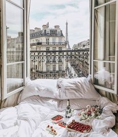 a bed with white sheets and pillows in front of an open window overlooking the eiffel tower