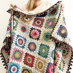 a woman is holding up a crocheted blanket