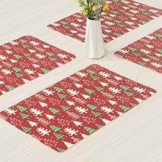 four red and green christmas themed placemats with flowers in a vase on the floor