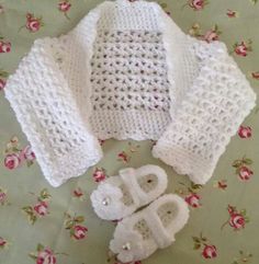 a crocheted sweater and booties sitting on top of a flowered tablecloth