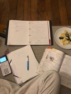 an open notebook, calculator and cell phone sitting on a table with food