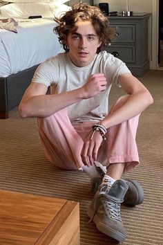 a young man sitting on the floor in front of a bed