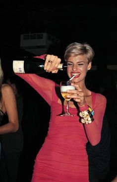 a woman in a red dress holding a wine glass and pouring it into her mouth