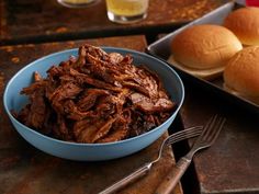 a bowl of pulled pork next to two buns