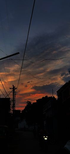 the sun is setting behind power lines and telephone poles in an urban area with cars parked on the street