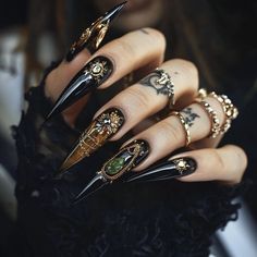 Discover the epitome of luxury in gothic nail art with these sharp, black stiletto nails. Adorned with intricate gold details and a bold emerald gem, this nail design is perfect for those who crave a blend of dark elegance and opulence. Ideal for making a statement with your manicure. Black Nails Press On, Ornate Nails, Black Vampire Nails, Stilettos Nails Designs, Black And Gold Halloween Nails, Black Gothic Nails, Dark Elegant Nails, Nails Black And Gold, Gothic Nails Stiletto