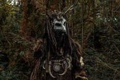 a man with dreadlocks standing in front of some trees and bushes wearing a costume