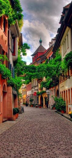 an alley way with buildings and trees on both sides, surrounded by cobblestones