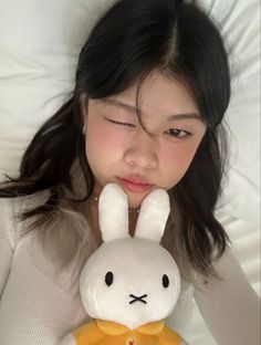 a woman laying in bed with a stuffed animal rabbit on her lap and looking at the camera