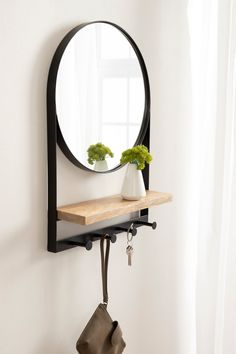 a round mirror hanging on the wall above a shelf with a potted plant in it