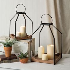 two metal lanterns with lit candles on top of them next to a potted plant