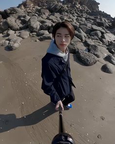 a young woman standing on top of a sandy beach next to the ocean holding a metal object