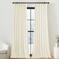 a white curtain hanging in front of a window next to a chair and potted plant