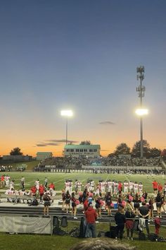 a group of people standing on top of a field next to a football field at sunset