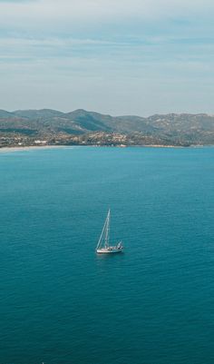 a sailboat floating on the ocean with mountains in the background