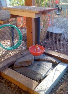 a red bowl sitting on top of a piece of wood next to a bird feeder