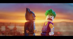 two lego batmans standing next to each other in front of a cityscape