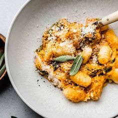 a white bowl filled with pasta covered in cheese and herbs next to a wooden spoon