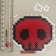 a red and black beaded skull sticker next to a ruler