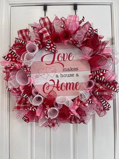 a pink and red valentine's day wreath hanging on a white door with the words love makes a house a home