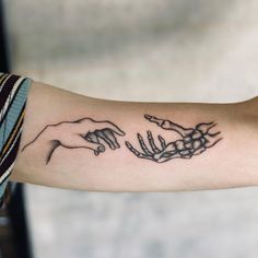 two hands touching each other with the creation behind them tattoo on left forearm and right arm