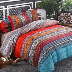 a bed with colorful comforters and pillows on top of it in a room next to a plant