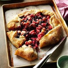 a pie with fruit on it sitting on top of a pan next to a knife